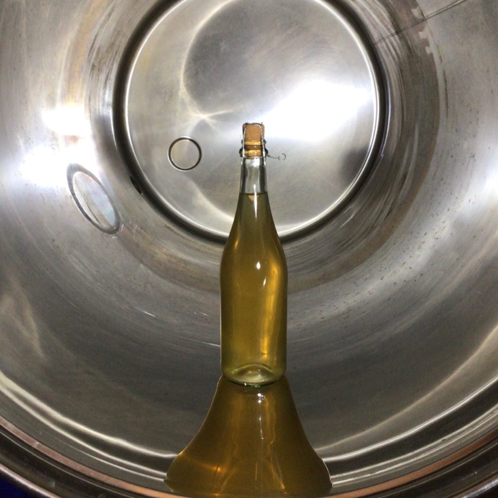 Bottle of Perry inside stainless steel fermenting tank